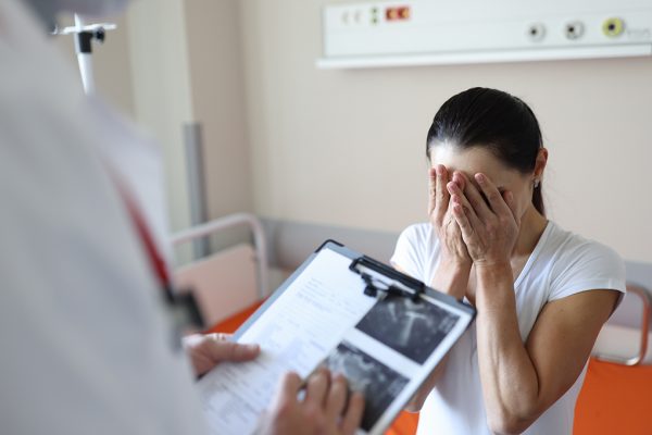 Doctor holding documents in front of crying patient in clinic. Psychological support for people with cancer concept